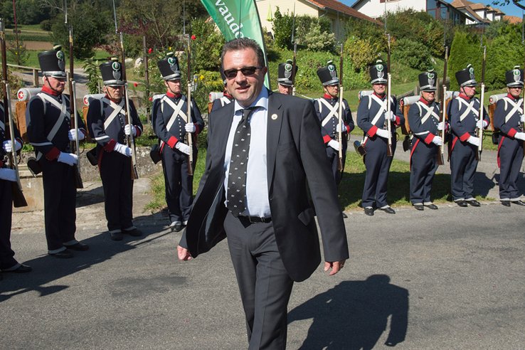 Jacques Nicolet porte des lunettes de soleil. Derrière, les Milices vaudoises en uniforme.