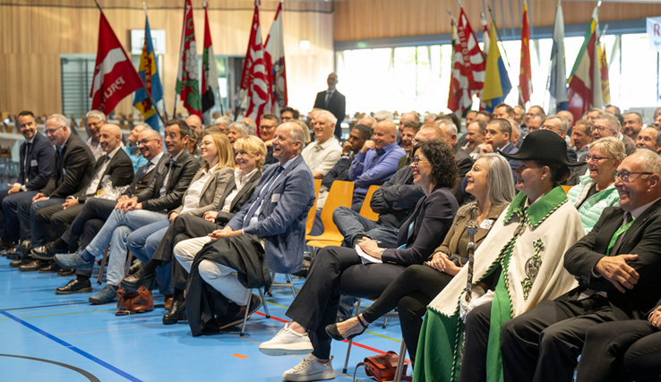plusieurs membres du Conseil d'Etat ainsi que des invités assis, assitent à un discours et rient.