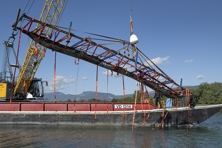 la pirogue, portée par des sangles, hissée hors de l'eau par la grue d'une barge