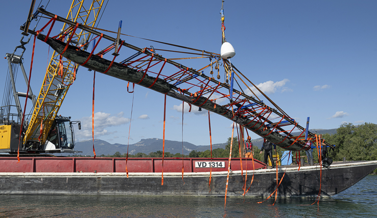 la pirogue, portée par des sangles, hissée hors de l'eau par la grue d'une barge