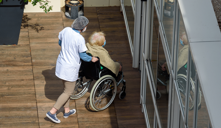 Aide médicale poussant une aînée en chaise roulante dans un EMS.