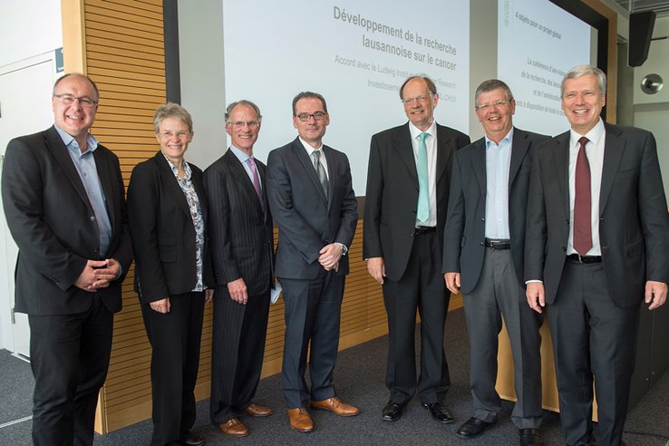 Les sept personnages posent. Dans leur dos, des écrans où apparaissent partiellement des messages de la conférence de presse.