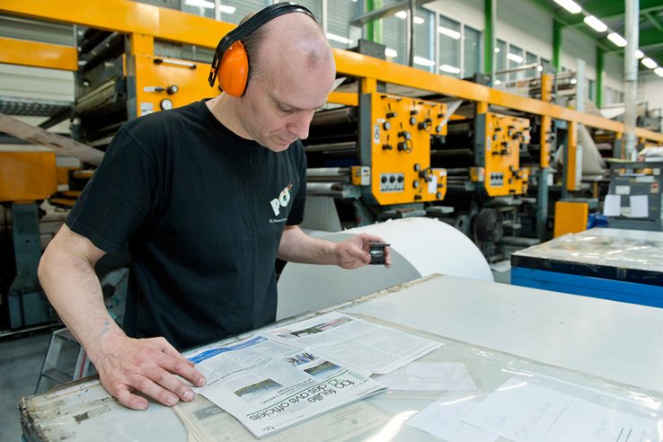Un rotativiste scrute une épreuve à l'aide d'un compte-fils. Derrière, la rotative.
