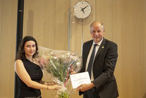 Les deux personnes posent devant l'horloge du Parlement. monsieur Thuillard remet une enveloppe à madame verboux.