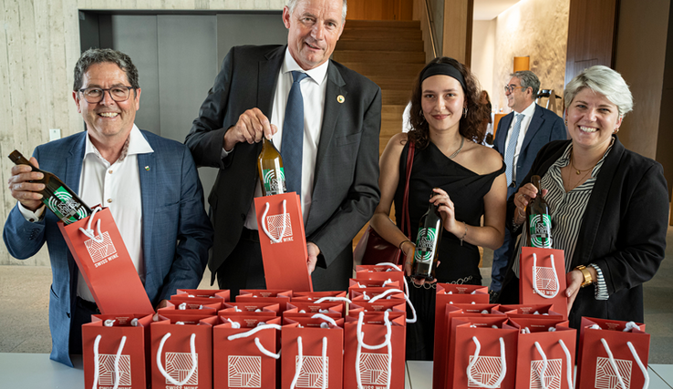 Les personnages posent derrière une table où sont déposées de nombreuses bouteilles emballées dans des sachets-cadeaux.