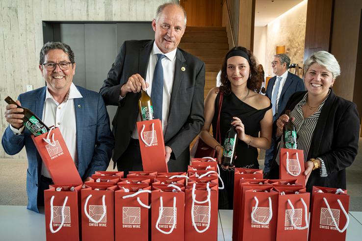 Les personnages posent derrière une table où sont déposées de nombreuses bouteilles emballées dans des sachets-cadeaux.