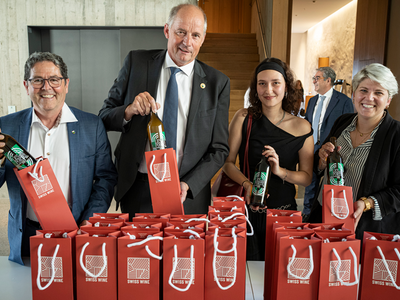 Les personnages posent derrière une table où sont déposées de nombreuses bouteilles emballées dans des sachets-cadeaux.