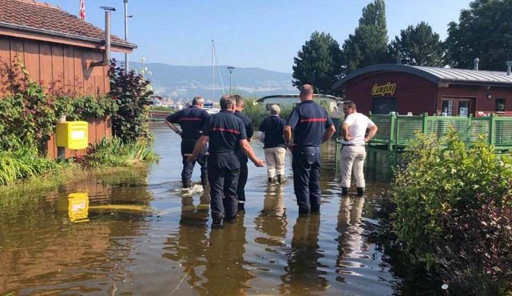 Plusieurs personnes avec de l'eau jusqu'au mollet dans un camping des rives du lac de Neuchâtel.