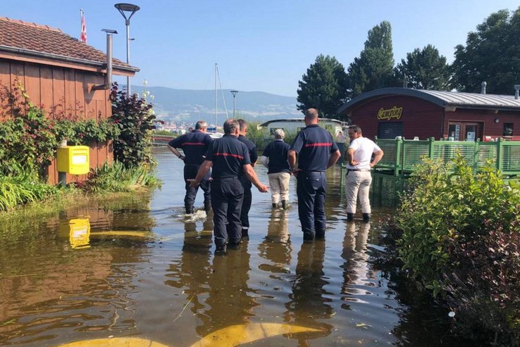 Plusieurs personnes avec de l'eau jusqu'au mollet dans un camping des rives du lac de Neuchâtel.