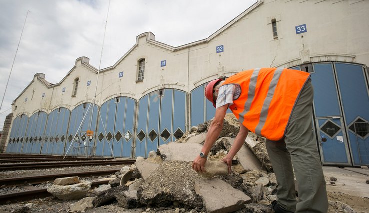Un ouvrier vêtu en orange travaille devant l'ancien dépôt des locomotives.