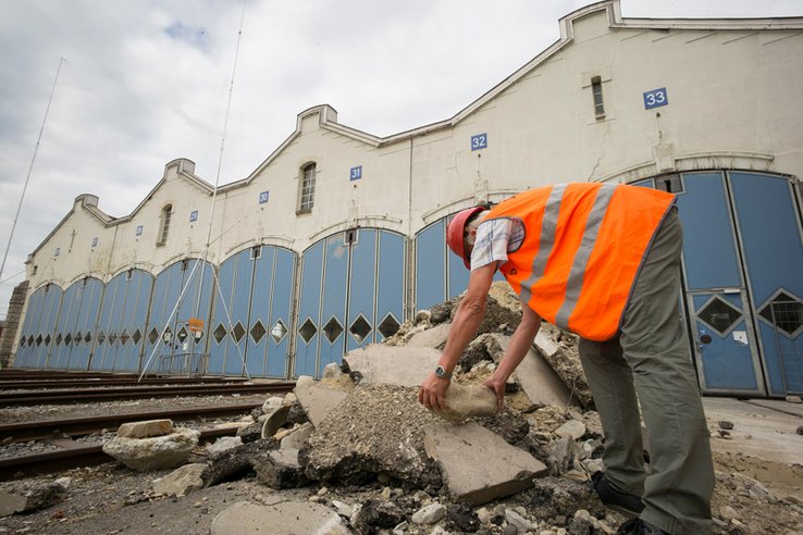 Un ouvrier vêtu en orange travaille devant l'ancien dépôt des locomotives.