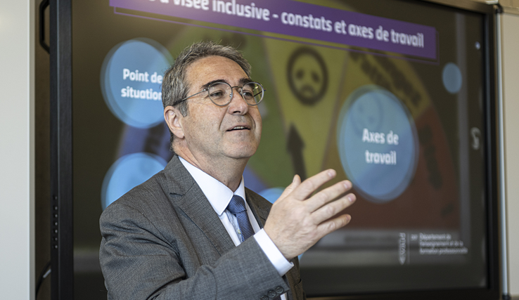 Le conseiller d'Etat en conférence de presse, fait un geste en tandant la main droite vers ses interlocuteurs.