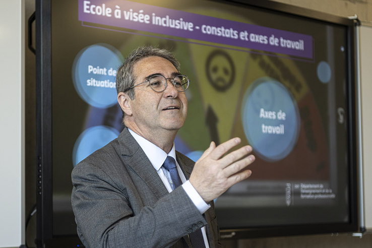 Le conseiller d'Etat en conférence de presse, fait un geste en tandant la main droite vers ses interlocuteurs.