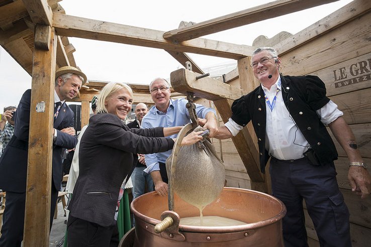 Les personnages sont autour d'un chaudron de fabrication de fromage, d'où l'on sort le caillé enveloppé d'une toile. Monsieur Bidau porte un chapeau de paille.