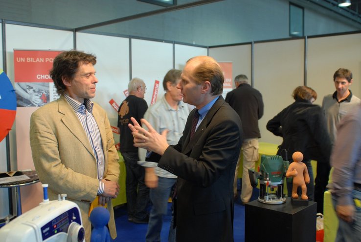Le conseiller d'Etat Philippe Leuba discute avec un spécialiste des mesures du marché du travail sur un stand.