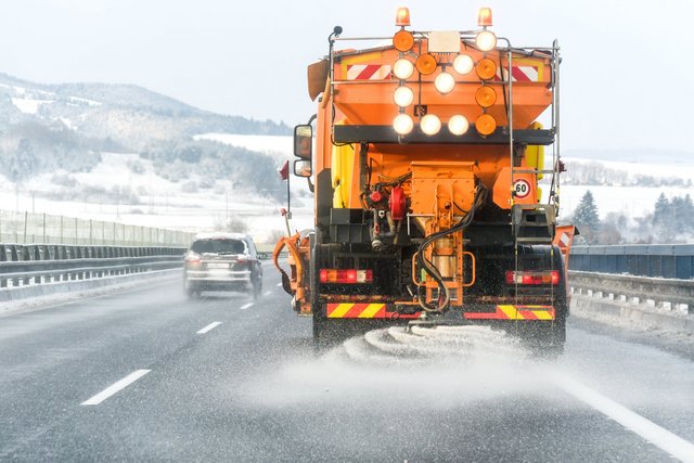 Snow plow on highway salting road. Orange truck deicing street. Salage