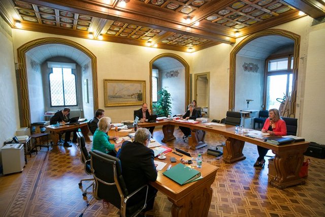 Les membres du Conseil d'Etat autour de la table en forme de U. Au fond de la pièce, le chancelier et la vice-chancelière.