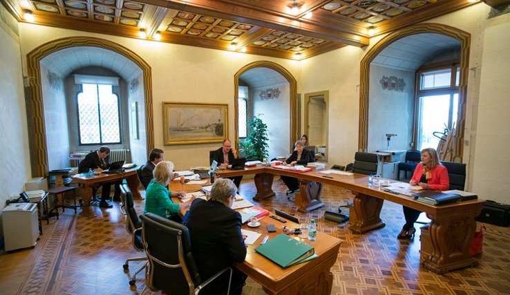 Les membres du Conseil d'Etat autour de la table en forme de U. Au fond de la pièce, le chancelier et la vice-chancelière.