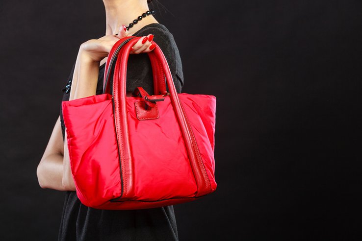 Femme dont on ne voit pas le visage tenant un grand sac rouge du bout des doigts.