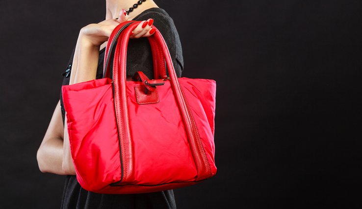 Femme dont on ne voit pas le visage tenant un grand sac rouge du bout des doigts.