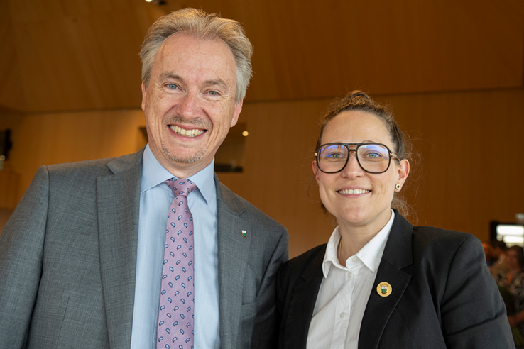 Les deux personnages en gros plan. Monsieur Miéville porte une cravate à motifs cachemire et madame Evéquoz un badge à l'écusson vaudois et ses larges lunettes rectangulaires.. 