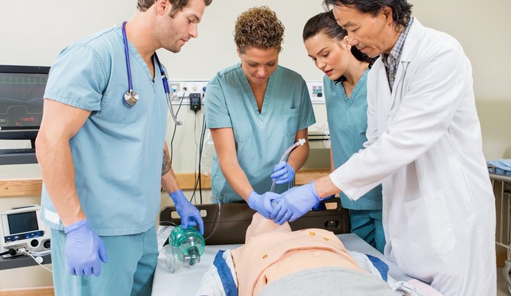 Des élèves infirmiers et un instructeur en tenue s'affairent autour d'un faux malade (poupée).