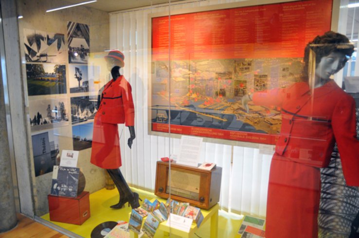 Vitrine de l'exposition des Archives cantonales: on voit notamment deux mannequins vêtus des costumes des hôtesses de l'Expo 64.