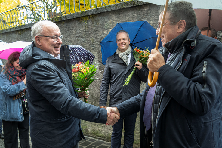 Les deux éus se serrent la main dans la rue, sous des parapluies et sous le regard de Raphaël Mahaim.