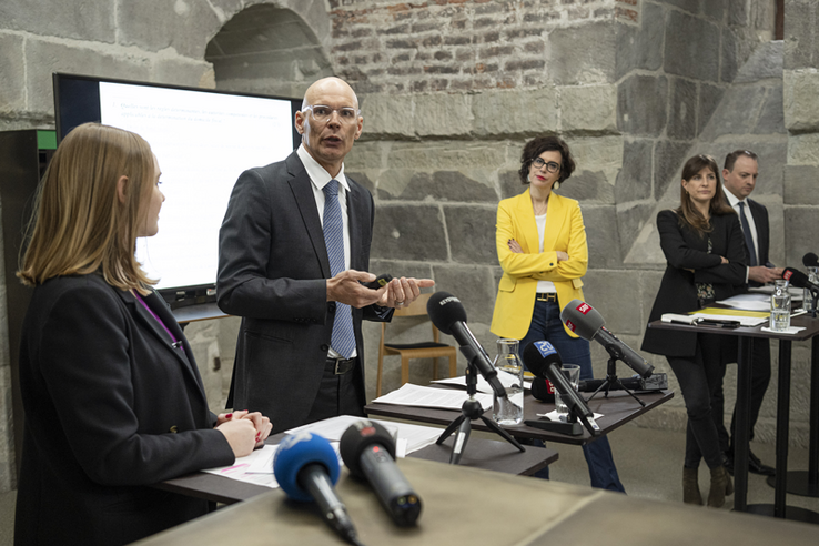 Me Daniel Schafer, avocat, expert fiscal diplômé, lors de la conférence de presse du 23 mars. L'avocat est au centre en train de parler, madame Dittli à gauche. La présidente du Conseil d'Etat Christelle Luisier, sa collègue Rebecca Ruiz et le chancelier Aurélien Buffat sont droite, plus au fond.