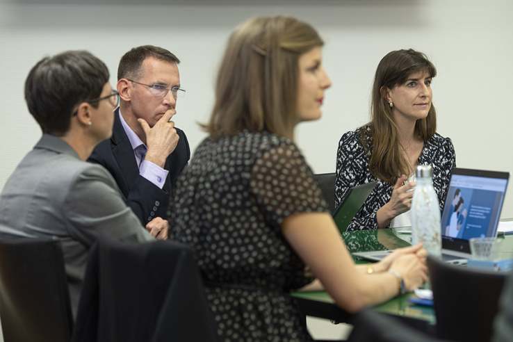 Les personnes sont assises autour d'une table durant la conférence de presse. Un ordinateur est ouvert sur la table.
