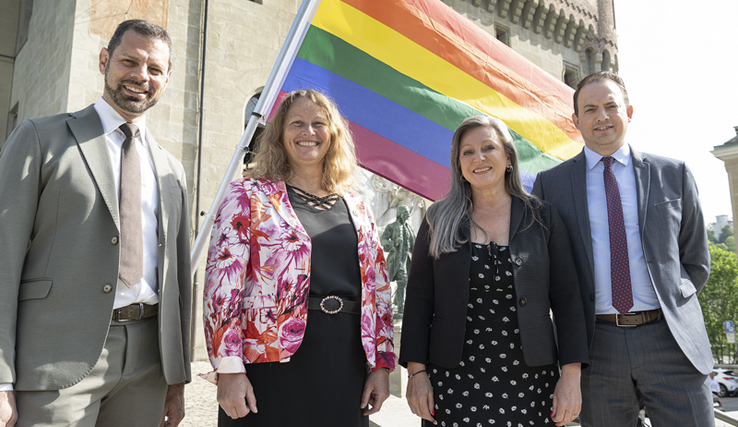 Les quatre personnes posent devant le drapeau arc-en-ciel, devant le château Saint-Maire..
