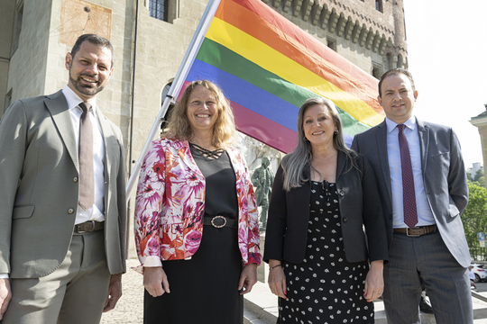 Les quatre personnes posent devant le drapeau arc-en-ciel, devant le château Saint-Maire..