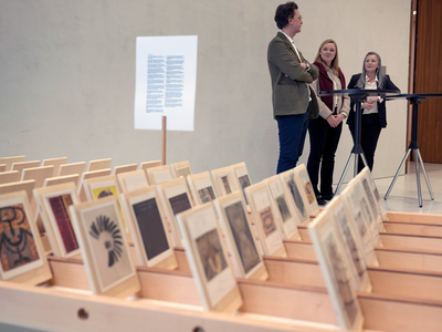 Les trois personnes bavardent au second plan, derrière une série d'images (sorte de cartes postales) des 130 oeuvres exposées.