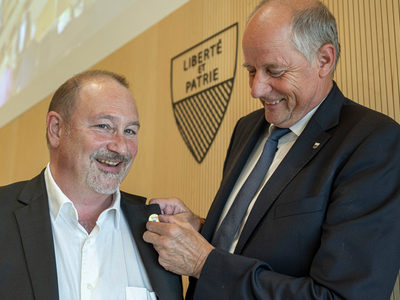 Monsieur Thuillard fixe un pins au revers du veston de son successeur.