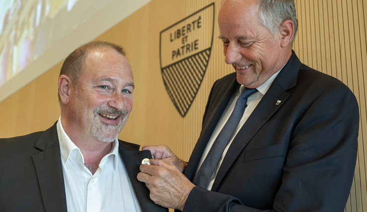 Monsieur Thuillard fixe un pins au revers du veston de son successeur.