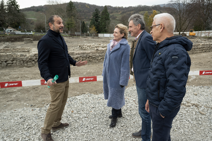 Les personnes écoutent l'archéologue cantonal. On voit à leurs coiffures que le vent souffle.