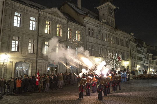 Les Milices vaudoises face à l'Hôtel de Ville de Lausanne, de nuit tirent en l'air avec leurs fusils des cartouches lumineuses. En face, des spectateurs se bouchent les oreilles.