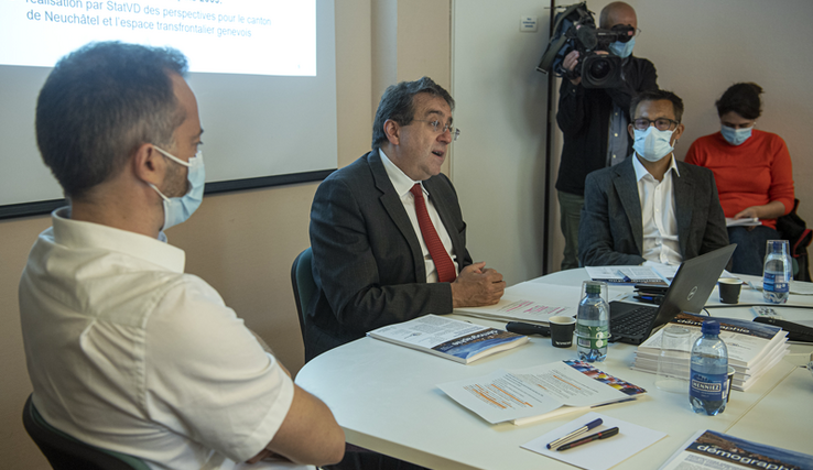 Les trois personnages en conférence de presse. Au fond, un cameraman et une journaliste.