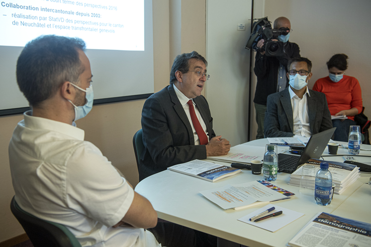 Les trois personnages en conférence de presse. Au fond, un cameraman et une journaliste.