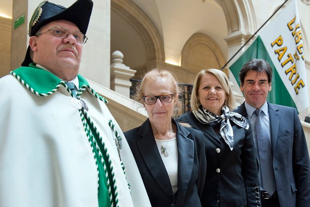 Les trois magistrats de la Cour des comptes dans l'atrium du Palais de Rumine, accompagné d'un huissier. Derrière eux, un drapeau vaudois.
