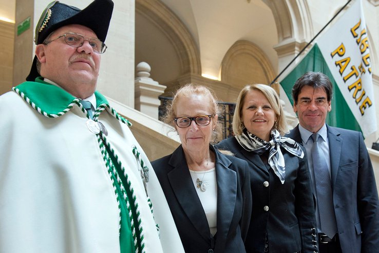 Les trois magistrats de la Cour des comptes dans l'atrium du Palais de Rumine, accompagné d'un huissier. Derrière eux, un drapeau vaudois.