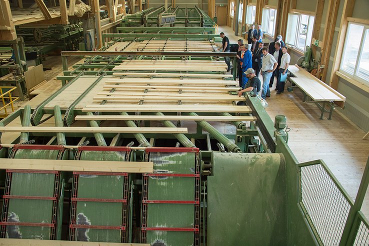 Le bois débité se présente sur une énorme machine. Les personnages, ouvriers et politiques, se tiennent sur le côté de ce train.
