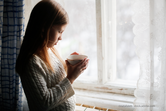 Une enfant au regard triste boit un thé à la fenêtre