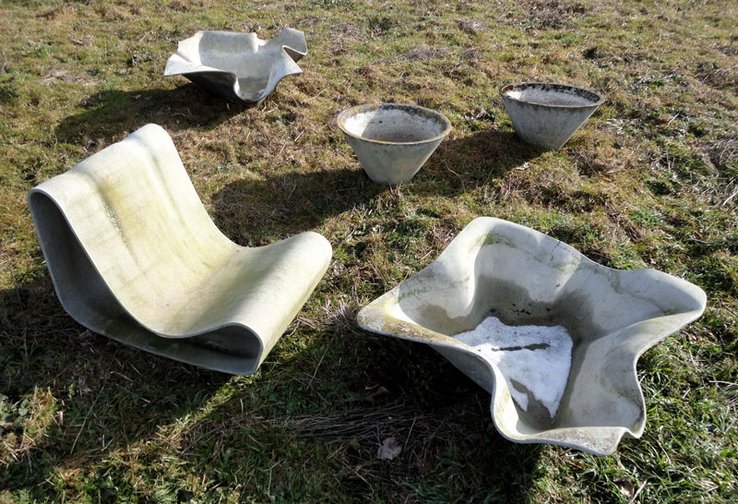 Un siège et différents types de bacs à fleurs posés sur une pelouse.