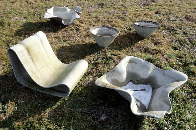 Un siège et différents types de bacs à fleurs posés sur une pelouse.