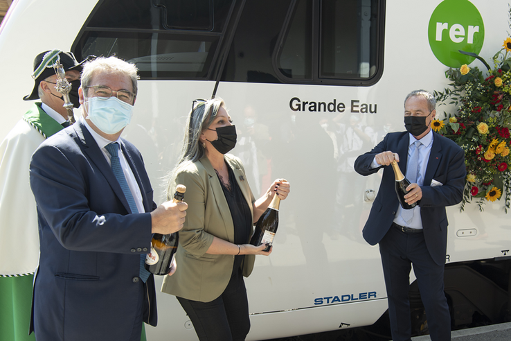Les trois personnages tiennent chacun une bouteille de champagne devant le train.