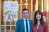 Les deux personnes posent à côté d'une affiche annonçant le colloque sur l'encouragement précoce