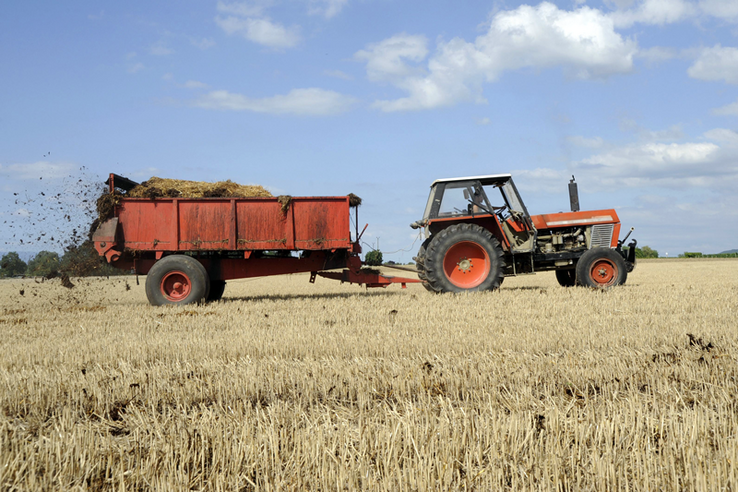 Un tracteur et une machine d'épandage du fumier en action dans un champ.