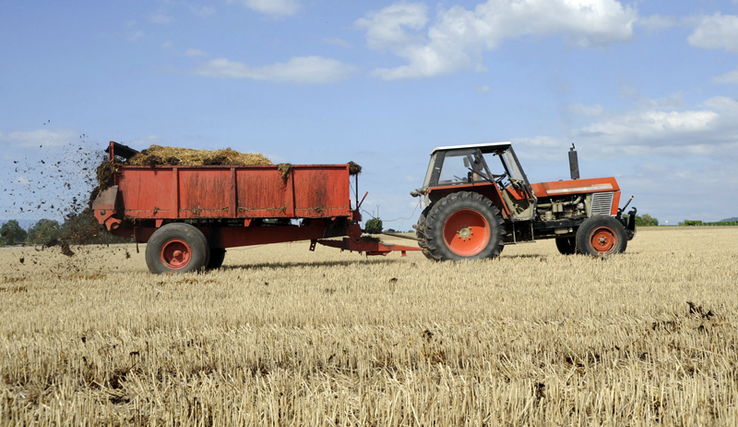 Un tracteur et une machine d'épandage du fumier en action dans un champ.