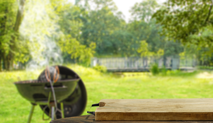 Un gril de type barbecue fume dans un espace vert en bordure de forêt